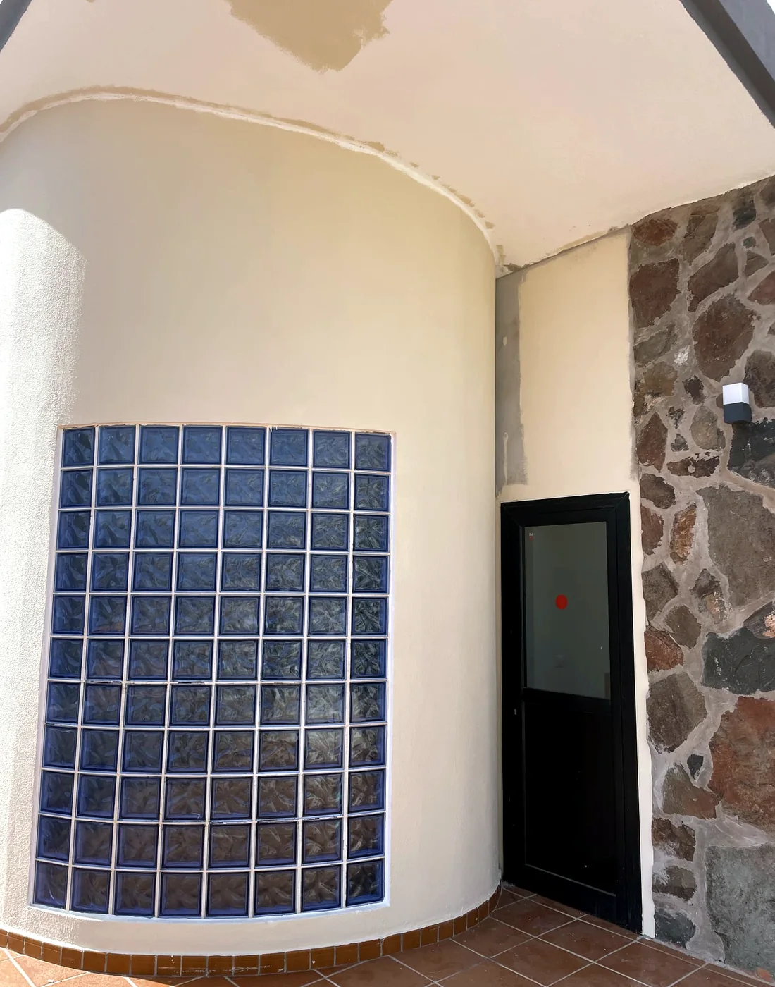 Property entrance with curved glass-block wall, black door, stone wall and terracotta paving
