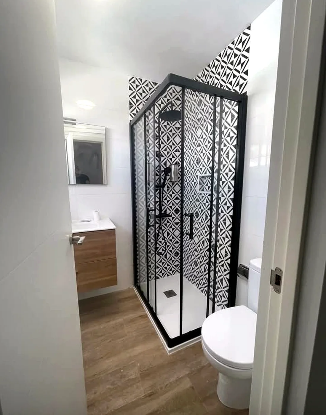 Bathroom with geometric black-and-white shower tiles, black-framed enclosure and timber-effect floor